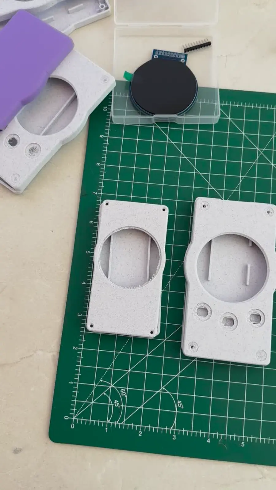 3D-printed badge shells and circular display module on a cutting mat