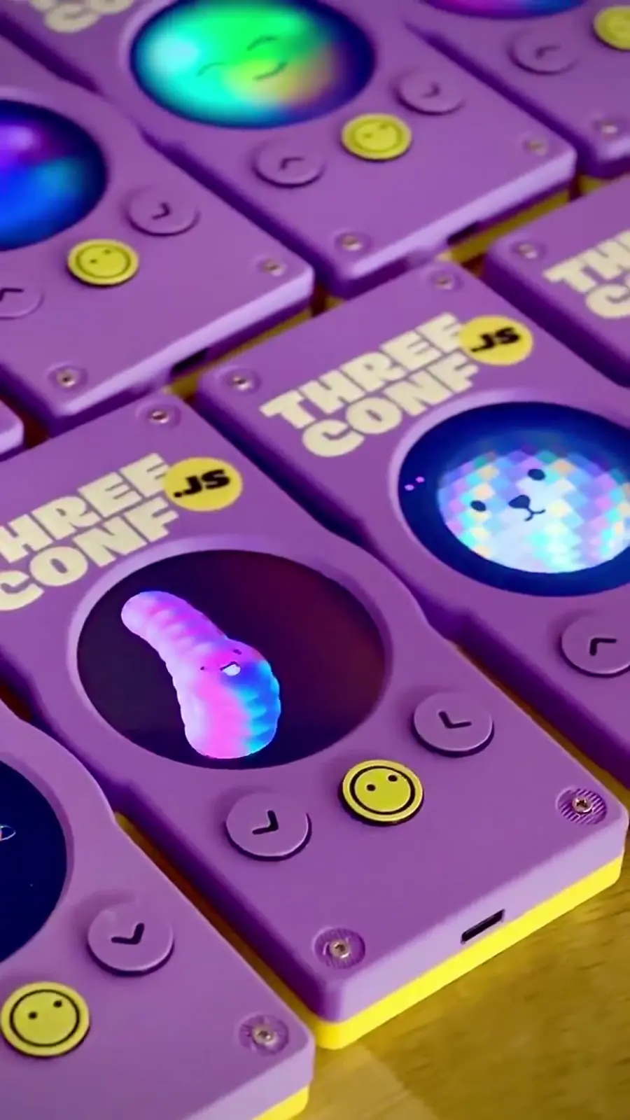 Close-up of purple and yellow Three.js Conf badges with animated screens